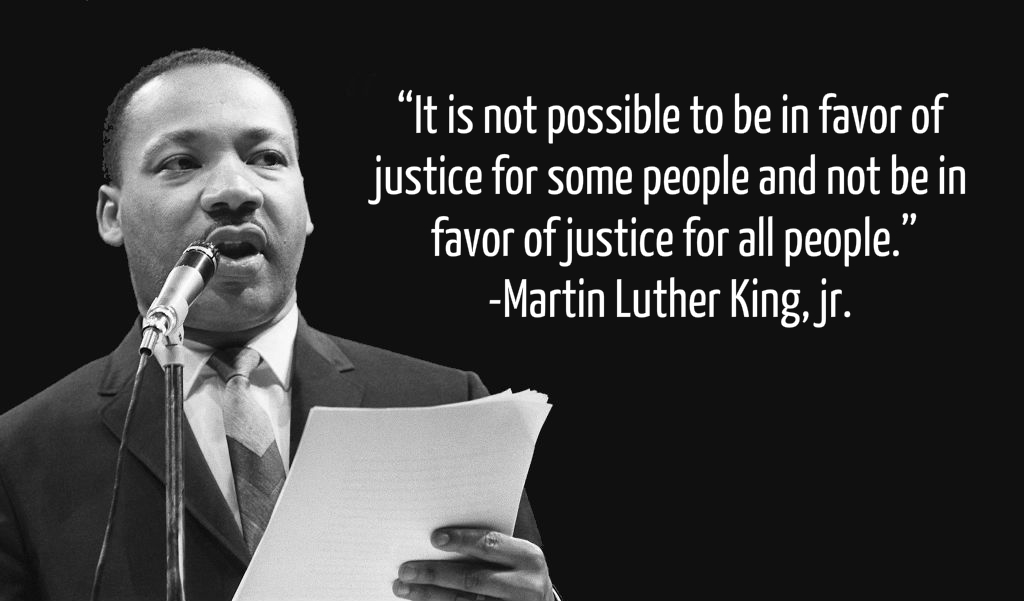 Martin Luther King Jr stands in front of microphone and text shows quote about importance of justice for all